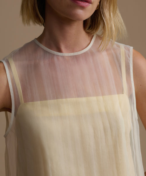 Woman wearing a sheer yellow cora top with a beige background