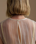 Back view of a woman wearing a yellow cora top with thin straps on a brown background