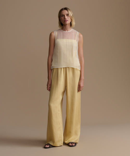 Woman wearing a light yellow cora top and wide-leg pants against a beige background