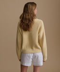 Woman wearing a yellow sweater and white shorts with blue stripes on a beige background