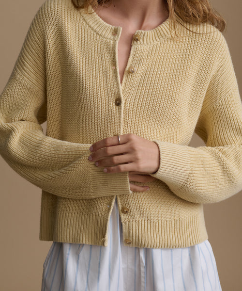 Person wearing a beige knitted cardigan against a neutral background