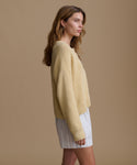 Woman wearing a light yellow sweater and white shorts against a beige background
