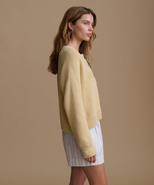 Woman wearing a light yellow sweater and white shorts against a beige background