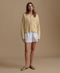 Woman wearing a yellow cardigan and stripe shorts on a beige background