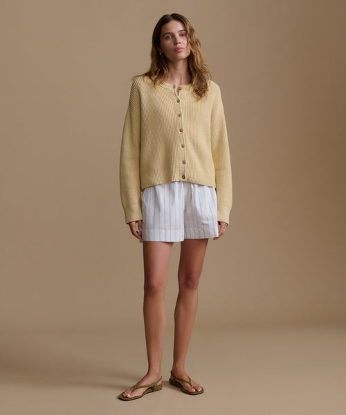 Woman wearing a yellow cardigan and stripe shorts on a beige background