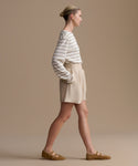 Woman wearing a striped shirt and beige shorts against a beige background