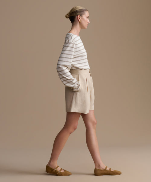 Woman wearing a striped shirt and beige shorts against a beige background