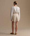 Woman wearing a striped shirt and beige shorts against a beige background