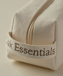 A close-up of The Travel Body Routine beige fabric pouch with a zipper and handle, featuring "Oak Essentials" in brown text. This minimalist pouch is ideal for carrying your skincare minis or TSA-approved travel essentials, shown on a neutral background.