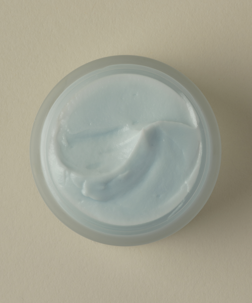 A top-down photo shows the Refining Mask—a round, open container of light blue mask—resting on a beige surface.