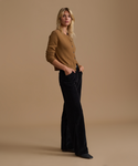 A model wearing a caramel cardigan with black corduroy pants against a beige studio background.