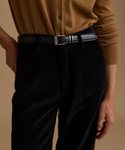 A model wearing a caramel cardigan with black corduroy pants against a beige studio background.