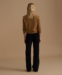 A model wearing a caramel cardigan with black corduroy pants against a beige studio background.