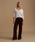 A model wearing an ivory sweater with burgundy corduroy pants against a beige studio background.