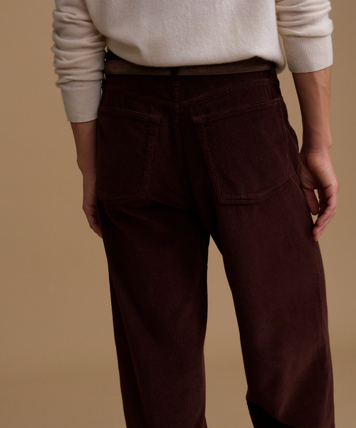A model wearing an ivory sweater with burgundy corduroy pants against a beige studio background.
