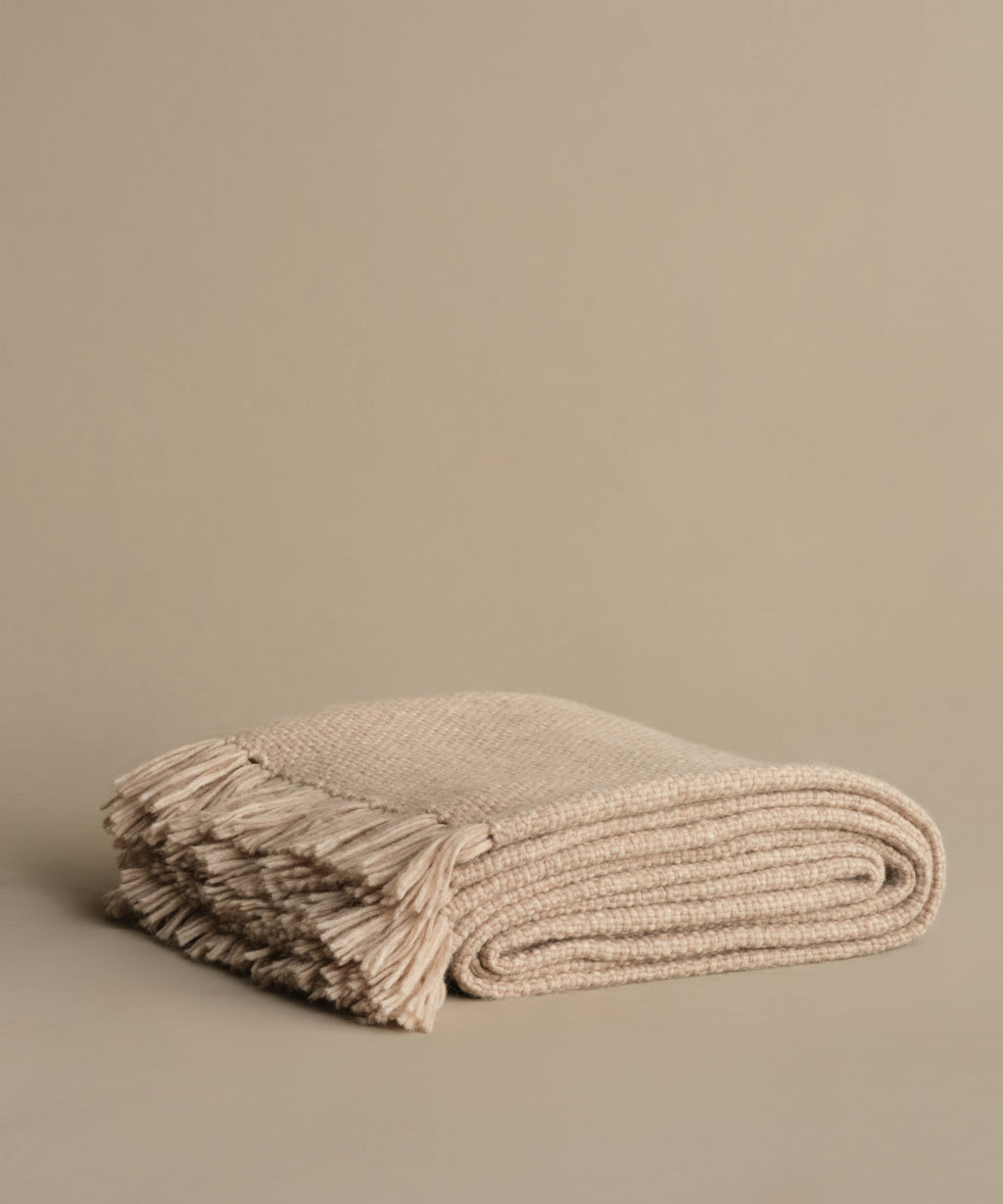 The Alpaca Basketweave Throw, handwoven in Peru from superfine alpaca and featuring fringed edges, is shown folded on a plain beige background.