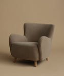 An accent chair upholstered in textured taupe fabric with light natural wood legs, set against a solid warm beige background.