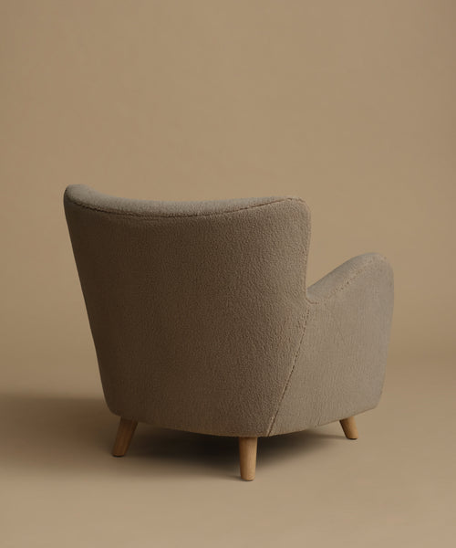 An accent chair upholstered in textured taupe fabric with light natural wood legs, set against a solid warm beige background.