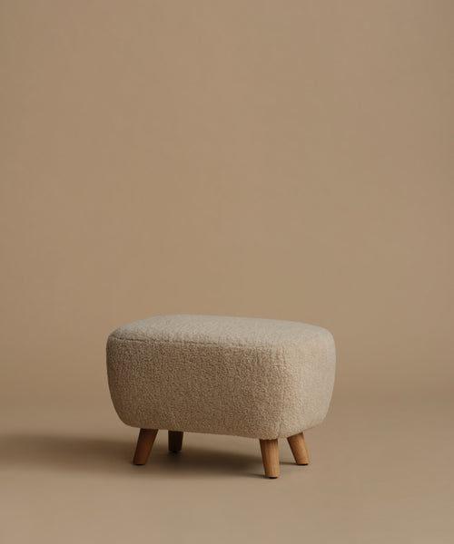 A low, square upholstered ottoman stool with a textured bouclé fabric in a light beige color and four tapered wooden legs, set against a solid warm beige background.