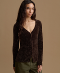 A woman modeling a dark brown ribbed knit cardigan with a V-neckline, paired with olive green pants, set against a solid warm beige background.