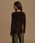 A woman shown from the back wearing a dark brown ribbed knit sweater and olive green pants, standing against a solid beige studio background.
