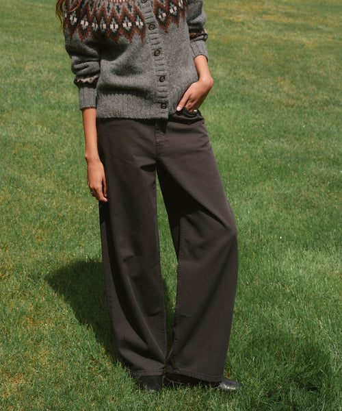 A person standing on green grass wearing dark charcoal wide-leg pants and a gray knit cardigan with a brown and cream pattern.