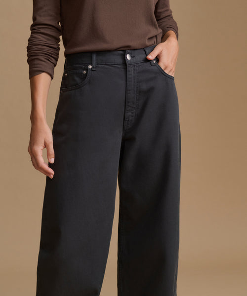A model wearing black wide-leg jeans and a brown long-sleeve top, standing against a solid beige background.