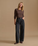 A woman modeling a dark brown long-sleeve crewneck top and black wide-leg jeans against a solid beige studio background.