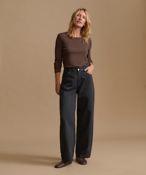 A woman modeling a dark brown long-sleeve crewneck top and black wide-leg jeans against a solid beige studio background.