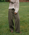 A person standing on a grassy lawn wearing wide-leg olive green pants and a cream knit sweater with a brown geometric pattern.