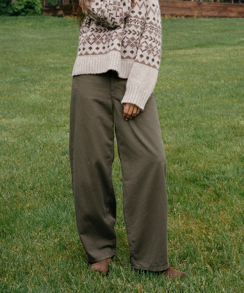 A person standing on a grassy lawn wearing wide-leg olive green pants and a cream knit sweater with a brown geometric pattern.
