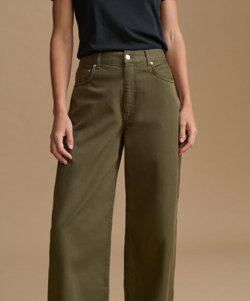 A model wearing olive green wide-leg jeans and a dark navy t-shirt, shown from the chest down against a solid beige studio background.