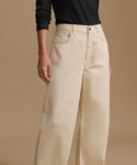 A model wearing high-waisted, wide-leg beige trousers and a black long-sleeve top, standing against a solid beige studio background.
