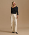 A woman modeling a black long-sleeve top and cream wide-leg trousers against a solid beige studio background.