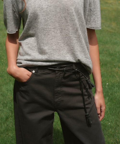 A person outside wearing a grey shirt with black pants and a black leather belt.