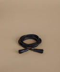 A coiled black wrap belt, photographed on a plain warm beige background.