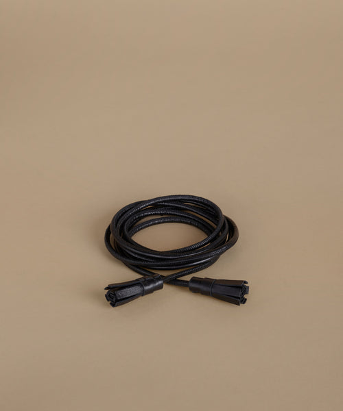 A coiled black wrap belt, photographed on a plain warm beige background.