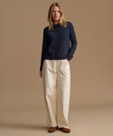 A woman modeling a dark navy ribbed knit sweater with long sleeves paired with cream wide-leg pants, against a solid warm beige studio background.