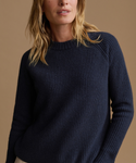 A woman wearing a dark navy ribbed knit sweater, shown from the chest up against a solid warm beige background.