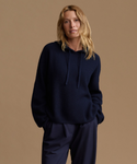 A woman modeling a dark navy ribbed knit hoodie with matching navy pants against a solid warm beige studio background.