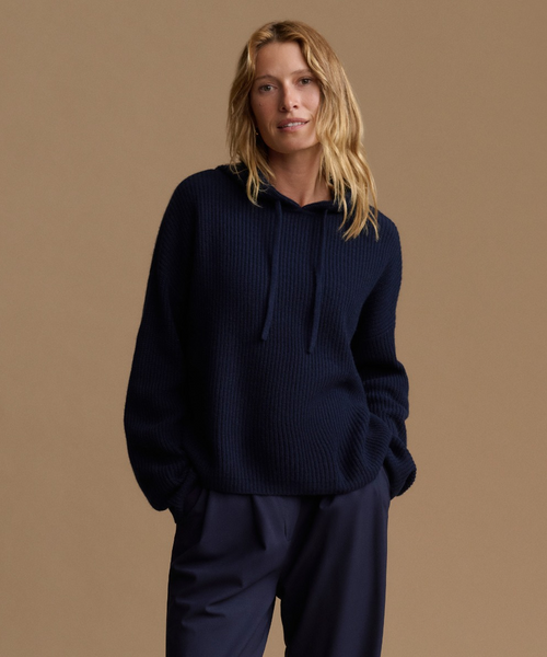 A woman modeling a dark navy ribbed knit hoodie with matching navy pants against a solid warm beige studio background.