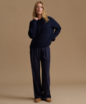 A woman modeling a matching navy blue knit hoodie and wide-leg sweatpants set against a solid beige studio background.