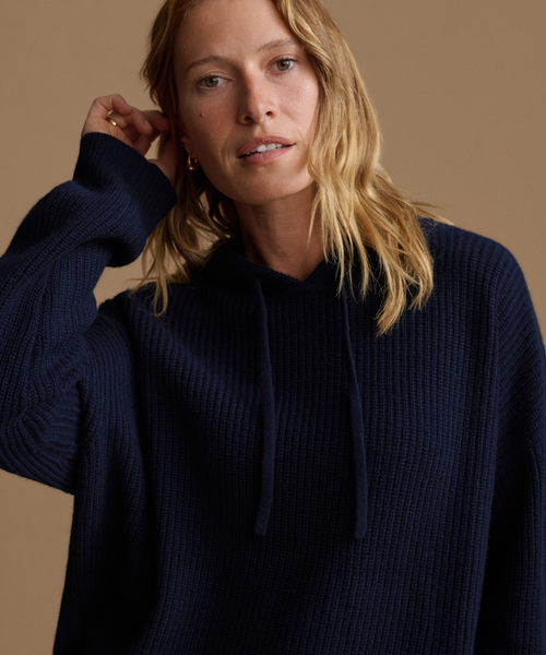 A woman wearing a navy blue waffle-knit hoodie with drawstrings, photographed against a solid warm beige background.