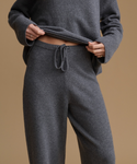 A person wearing a matching dark gray knit lounge set, featuring a long-sleeve top and drawstring pants, shown against a solid tan background.