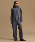 A woman modeling a dark gray knit two-piece loungewear set consisting of a mock-neck long-sleeve sweater and matching wide-leg trousers, set against a solid warm beige studio background.