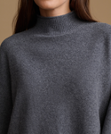 Close-up of a person wearing a dark gray ribbed mock neck sweater against a warm beige background.