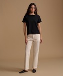 A woman modeling a black short-sleeve crewneck top and straight-leg cream pants against a solid warm beige studio background.