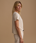 A model wearing a cream t-shirt with cream jeans against a beige studio background.