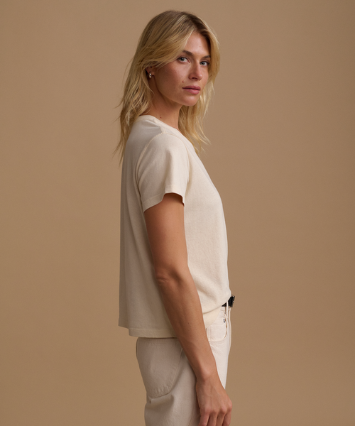 A model wearing a cream t-shirt with cream jeans against a beige studio background.