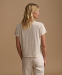 A model wearing a cream t-shirt with cream jeans against a beige studio background.